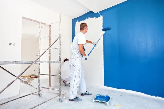 Pintor profesional aplicando pintura azul en una pared interior con andamio